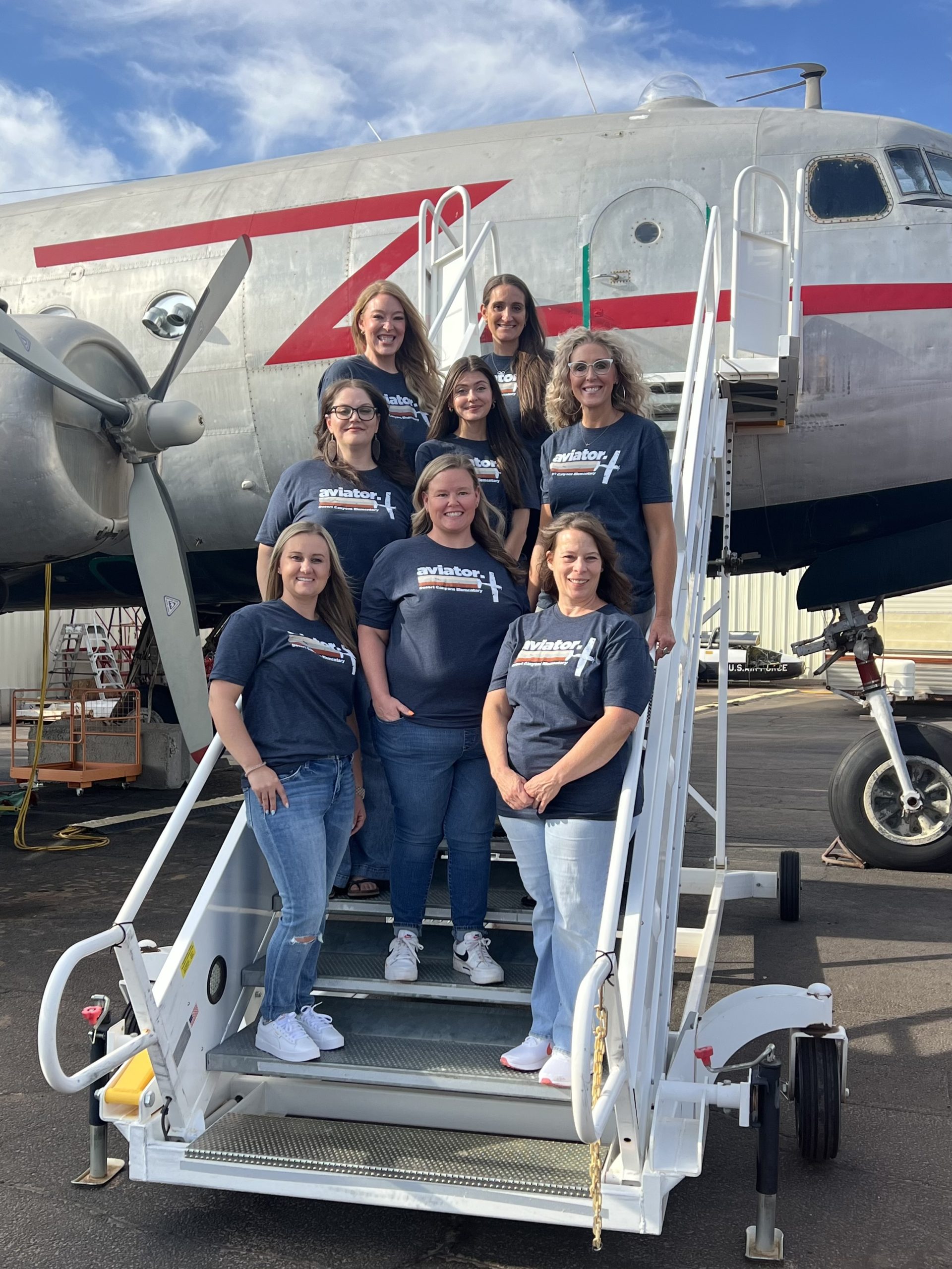 8 Women pose in front of a grey plane with a red strip on a movable staircase