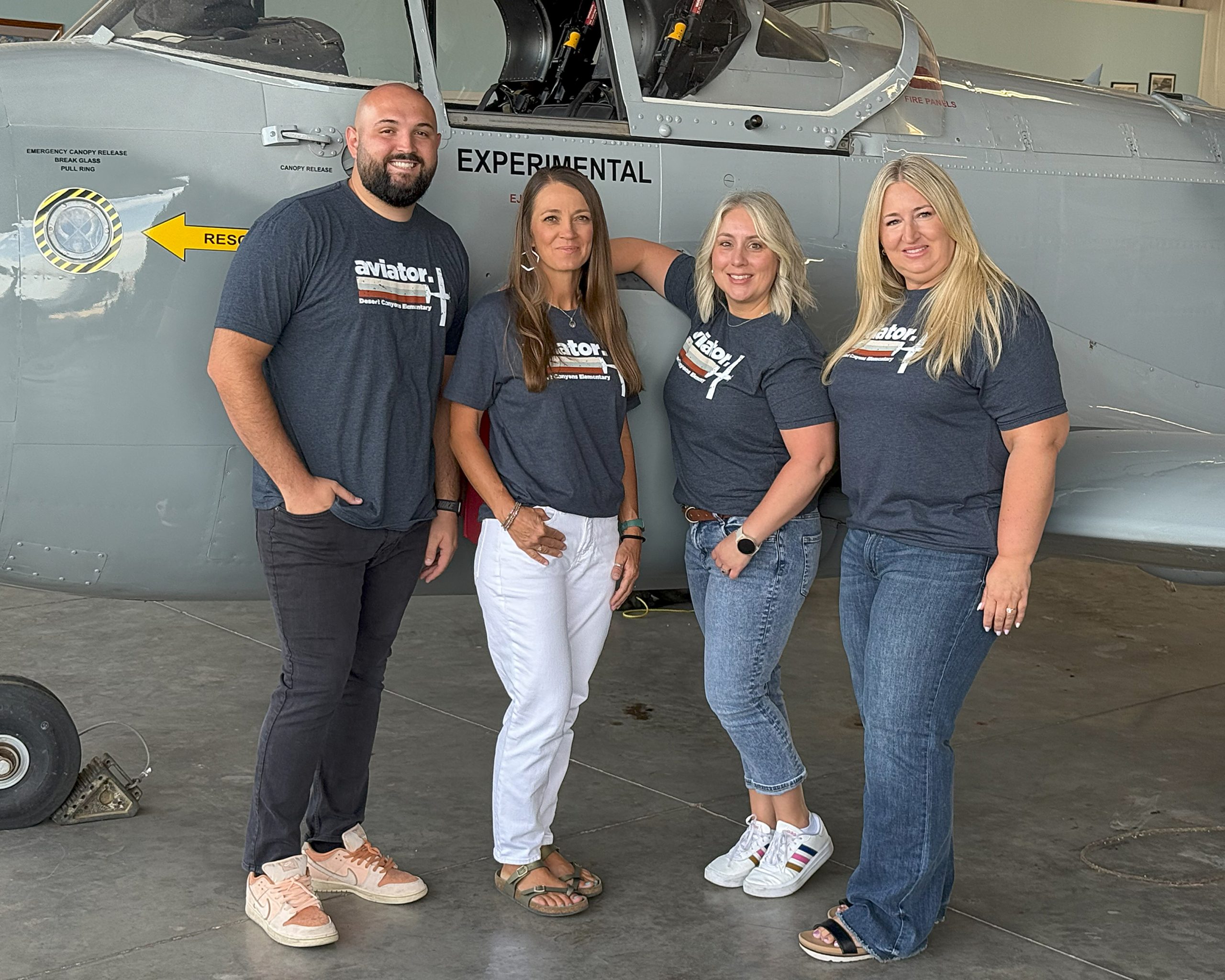 3 women and one man pose in front of a grey plane
