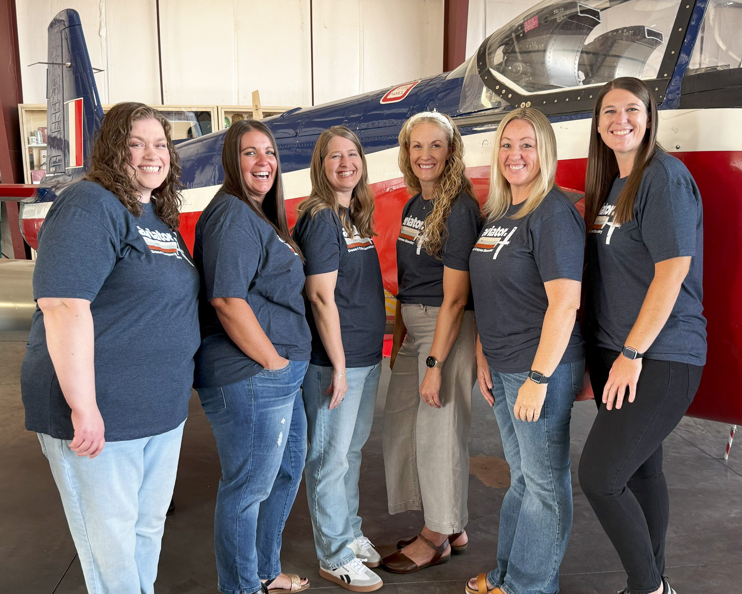 6 women pose in front of a red, white and blue plane