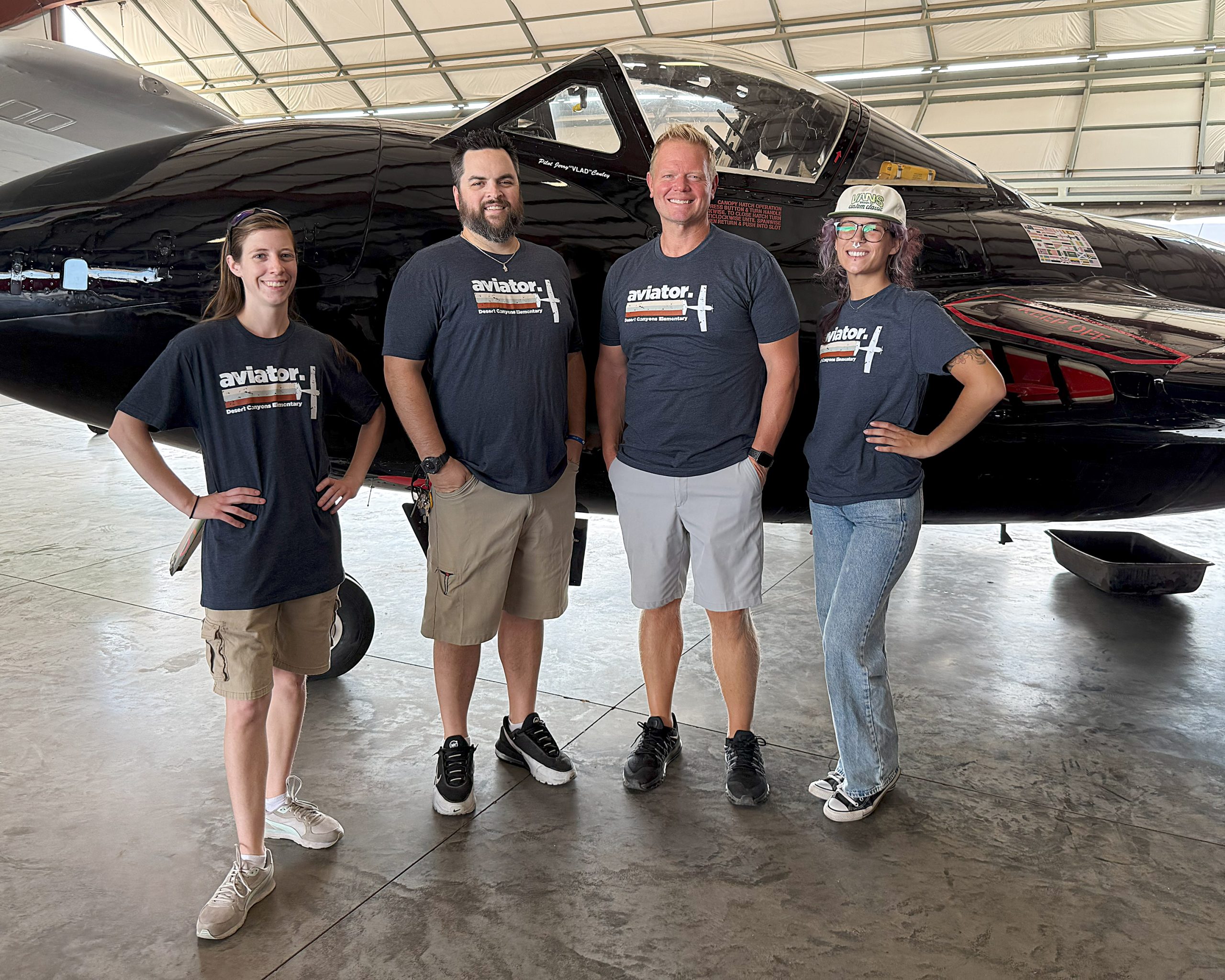 2 men and 2 women pose in front of a black airplane.