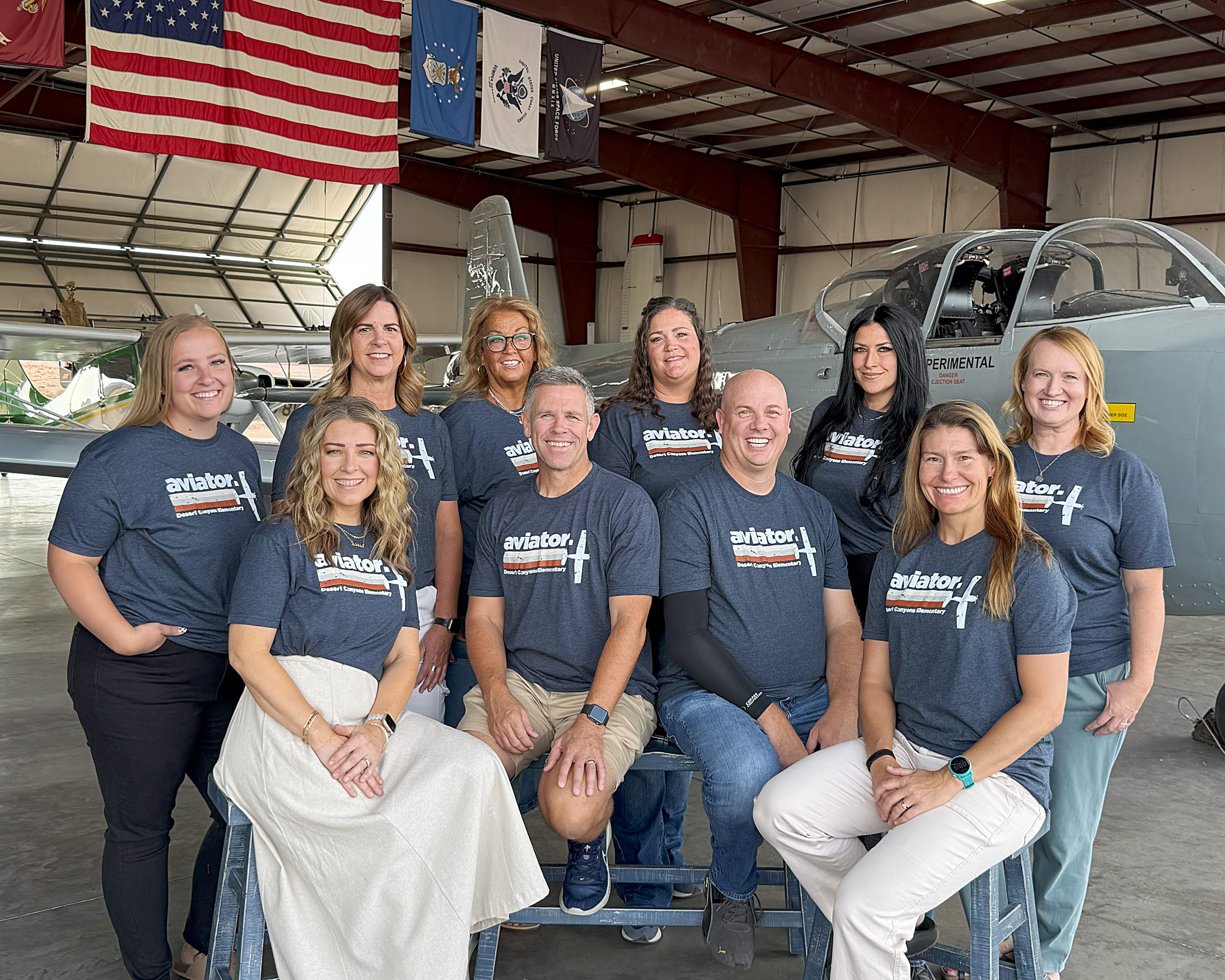 8 women and 2 men posed in front of an airplane in an airplane hangar.