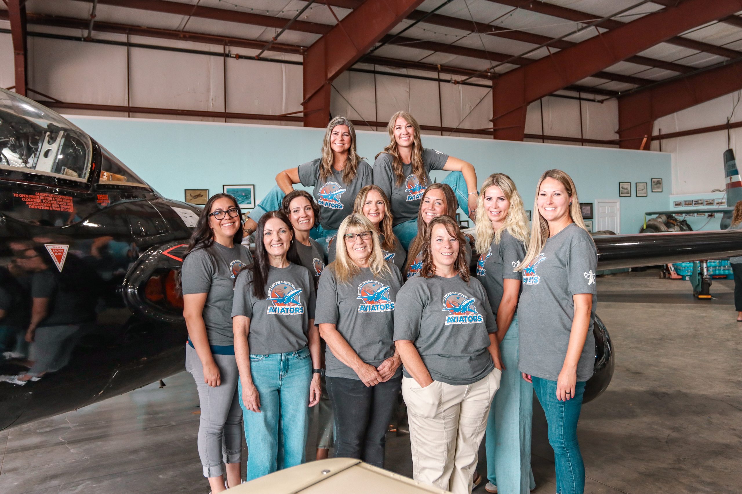 11 Women posing near an airplane with matching school t-shirts